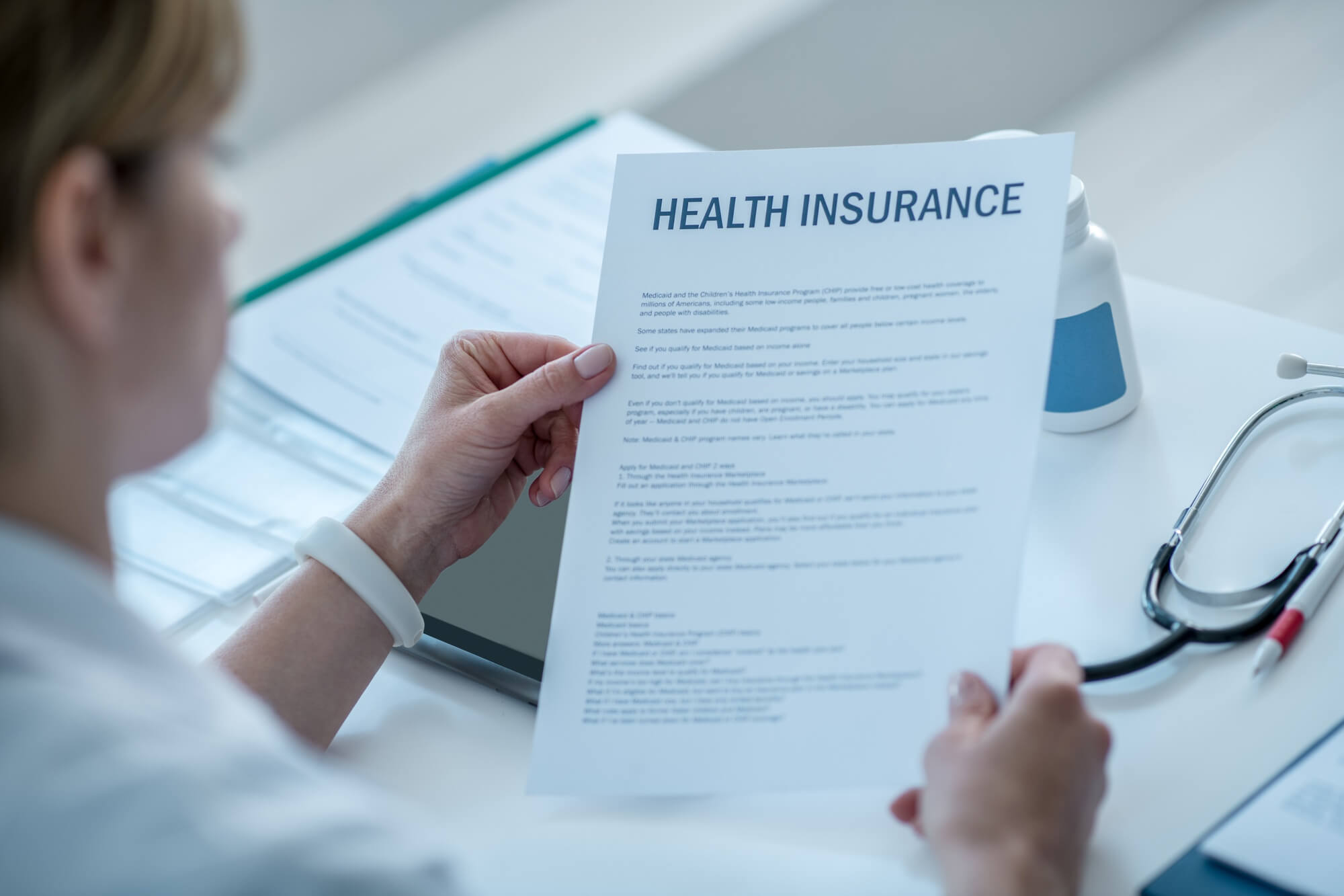 A person holding and reading a health insurance policy document at a desk, representing informed healthcare decisions.