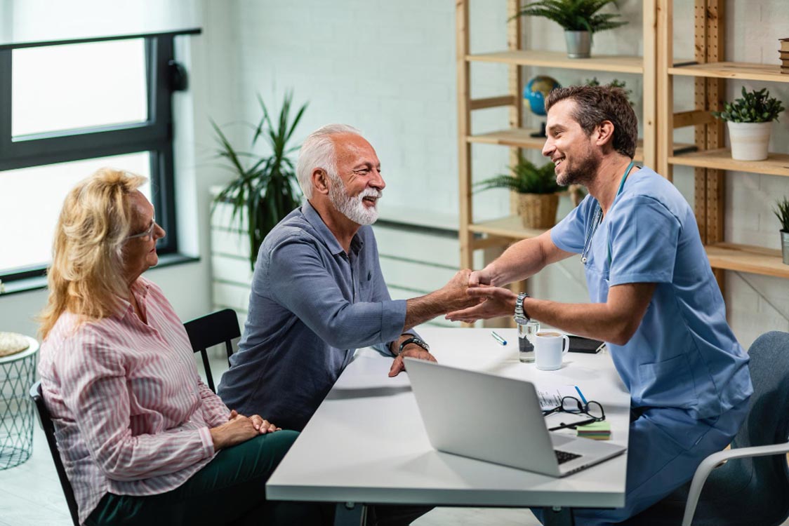Nurse or insurance advisor discussing health coverage with senior couple at a desk with a laptop in a bright office